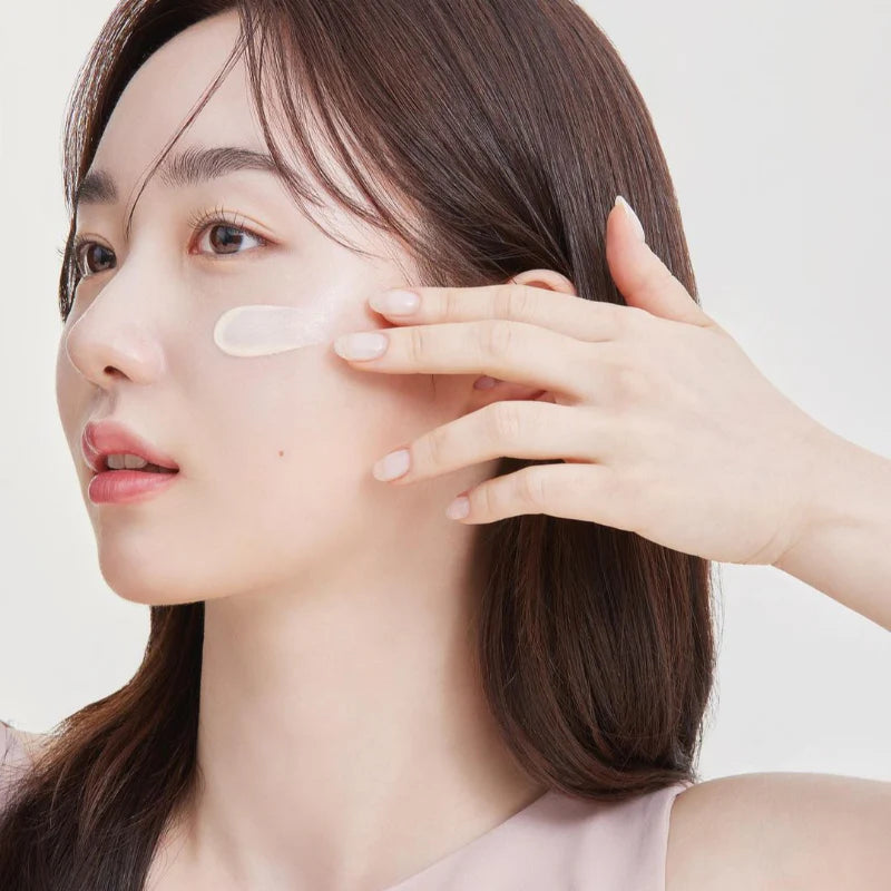 Woman applying suncream to her face with a neutral background