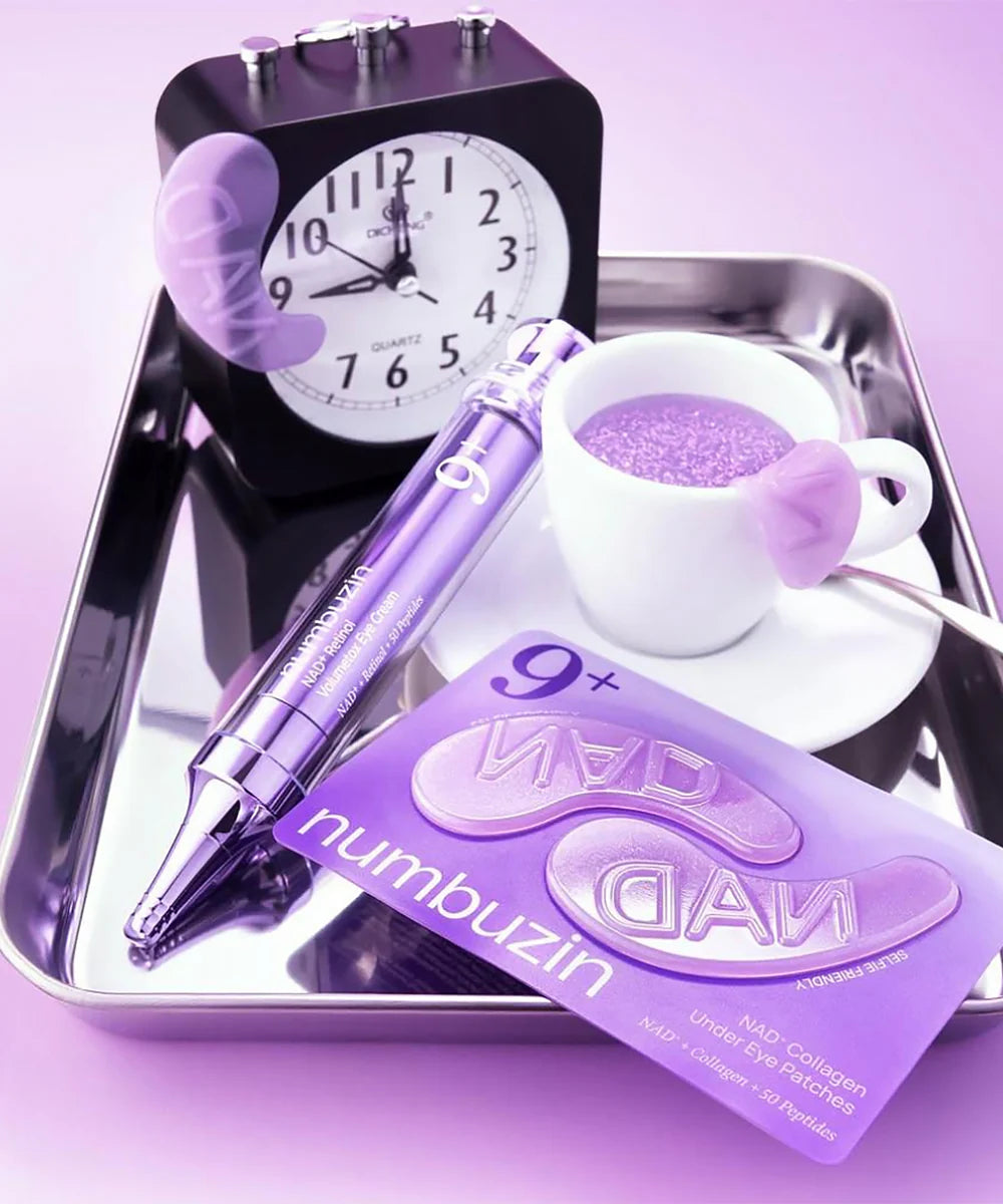 Numbuzin eye cream with a pen, clock, and cup on a tray against a purple background, also purple eye patches