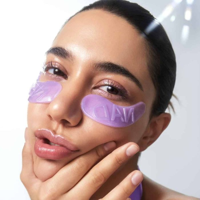 Woman wearing purple eye masks with a neutral background Numbuzin No.9 NAD+ Collagen Under Eye Patches 