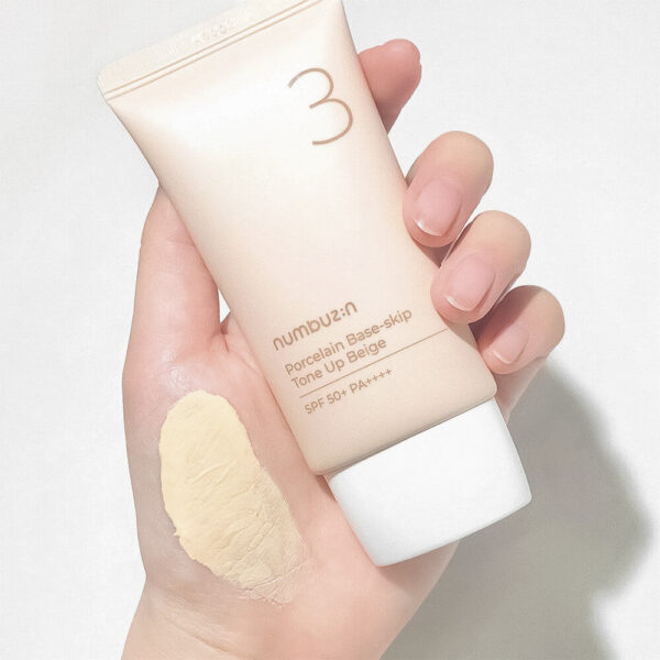 Hand holding a tube of num2un Porcelain Base-Skin Tone Up Benge with a swatch on the palm.