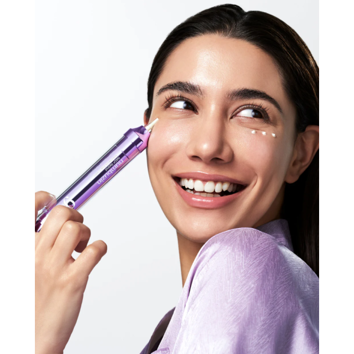 Woman applying a cosmetic numbuzin eye cream to her face with a purple applicator.